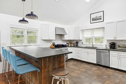 a kitchen with stainless steel appliances granite countertop a stove a refrigerator a sink a dining table and chairs with wooden floor