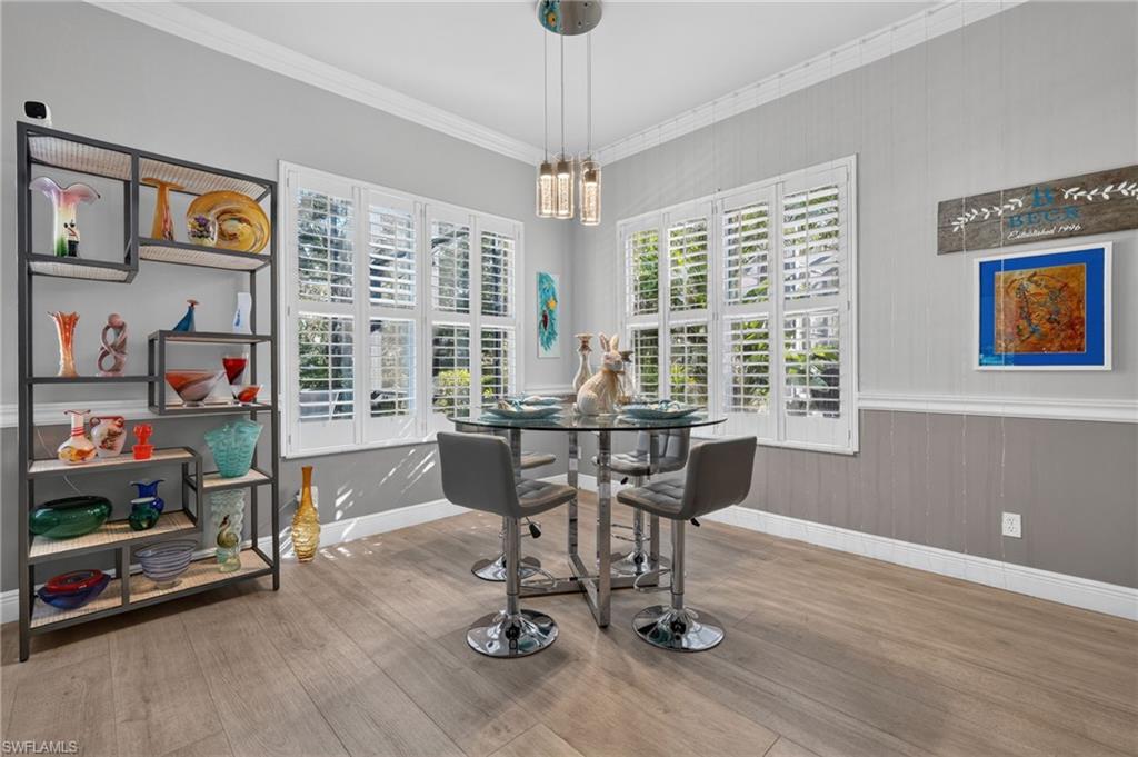 9970 Rookery Circle Estero, FL 33928 - Photo 19 of 50 Wood-finish flooring, white plantation shutters, decorative wall paneling, crown molding, and a modern pendant light fixture