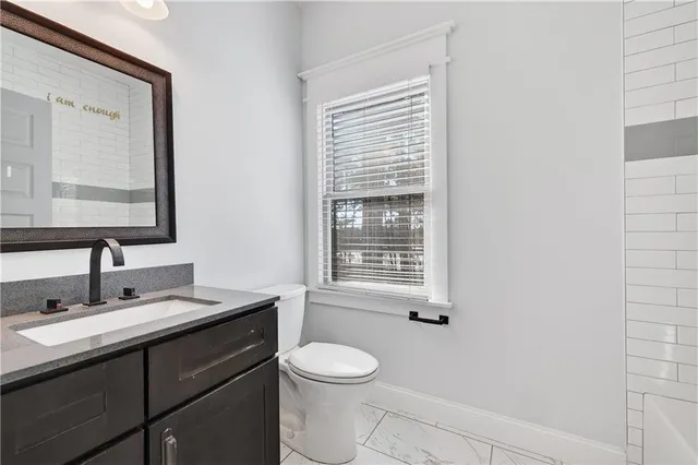 a bathroom with a toilet a sink a mirror a window and vanity