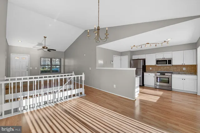 a open kitchen with stainless steel appliances granite countertop a refrigerator oven a sink dishwasher and white cabinets with wooden floor