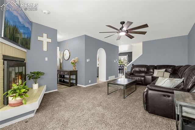 4990 Castledown Road Colorado Springs, CO 80917 - Photo 4 of 37 Carpeted living room with a tile fireplace, visible vents, arched walkways, baseboards, and ceiling fan