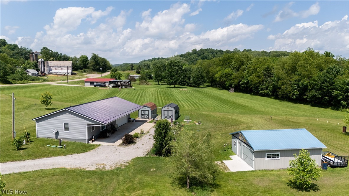 Expansive property featuring a light gray residence with a purple metal roof, a detached gray outbuilding with a blue metal roof, and two gray storage sheds with white trim