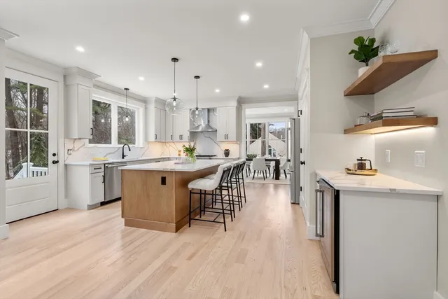 a kitchen with stainless steel appliances kitchen island granite countertop a sink a stove a refrigerator and white cabinets with wooden floor