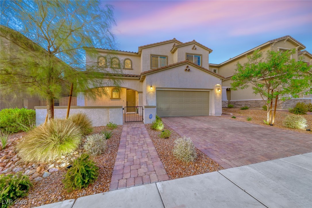 Mediterranean / spanish-style house with decorative paved driveway, a gate, stucco siding, and an attached garage
