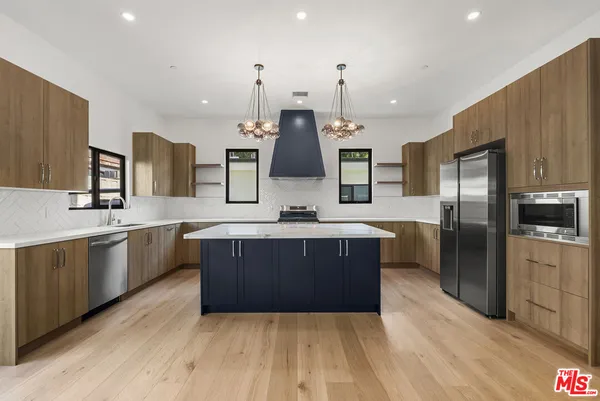 a large kitchen with a large counter top a sink stainless steel appliances and cabinets