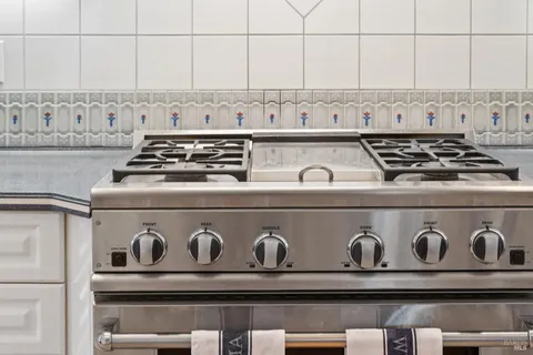 a kitchen with granite countertop a refrigerator a stove top oven a clock and wooden floor