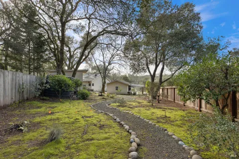 a backyard of a house with large trees and wooden fence