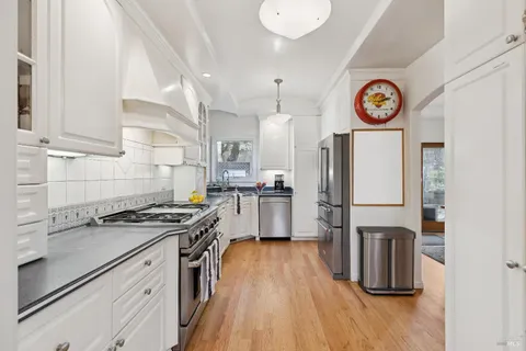 a kitchen with granite countertop a refrigerator a stove top oven a clock and wooden floor