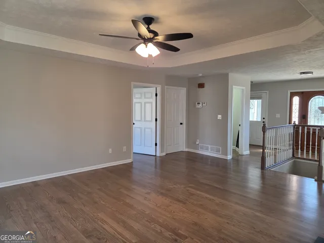 a view of an empty room with wooden floor and a ceiling fan