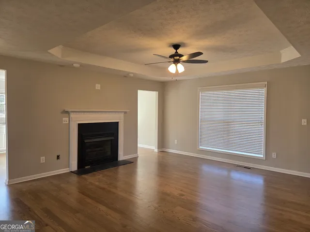 a view of an empty room with wooden floor fireplace and a window