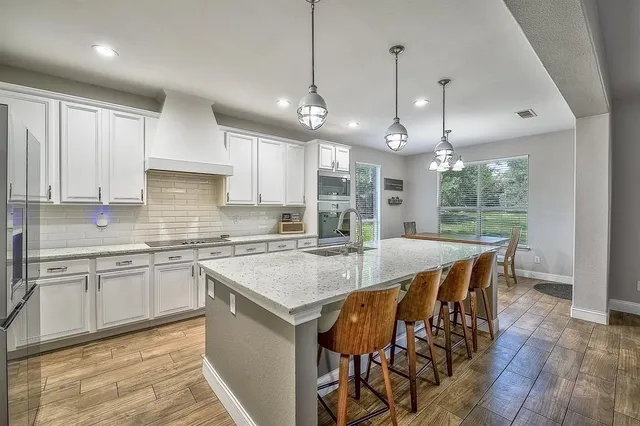 a large kitchen with stainless steel appliances a stove a sink dishwasher a refrigerator white cabinets and wooden floor