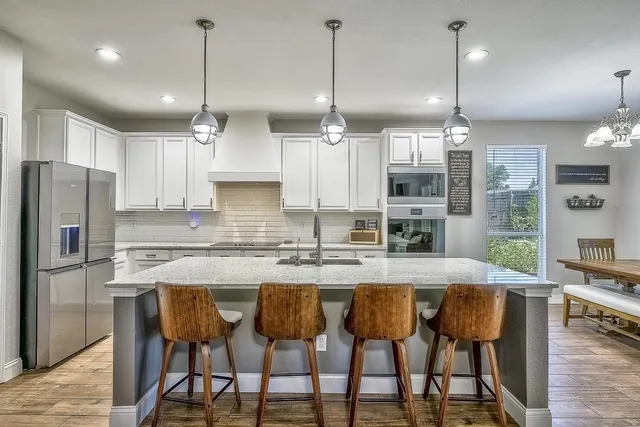 a kitchen with stainless steel appliances granite countertop a stove top oven a sink dishwasher a dining table and chairs with wooden floor