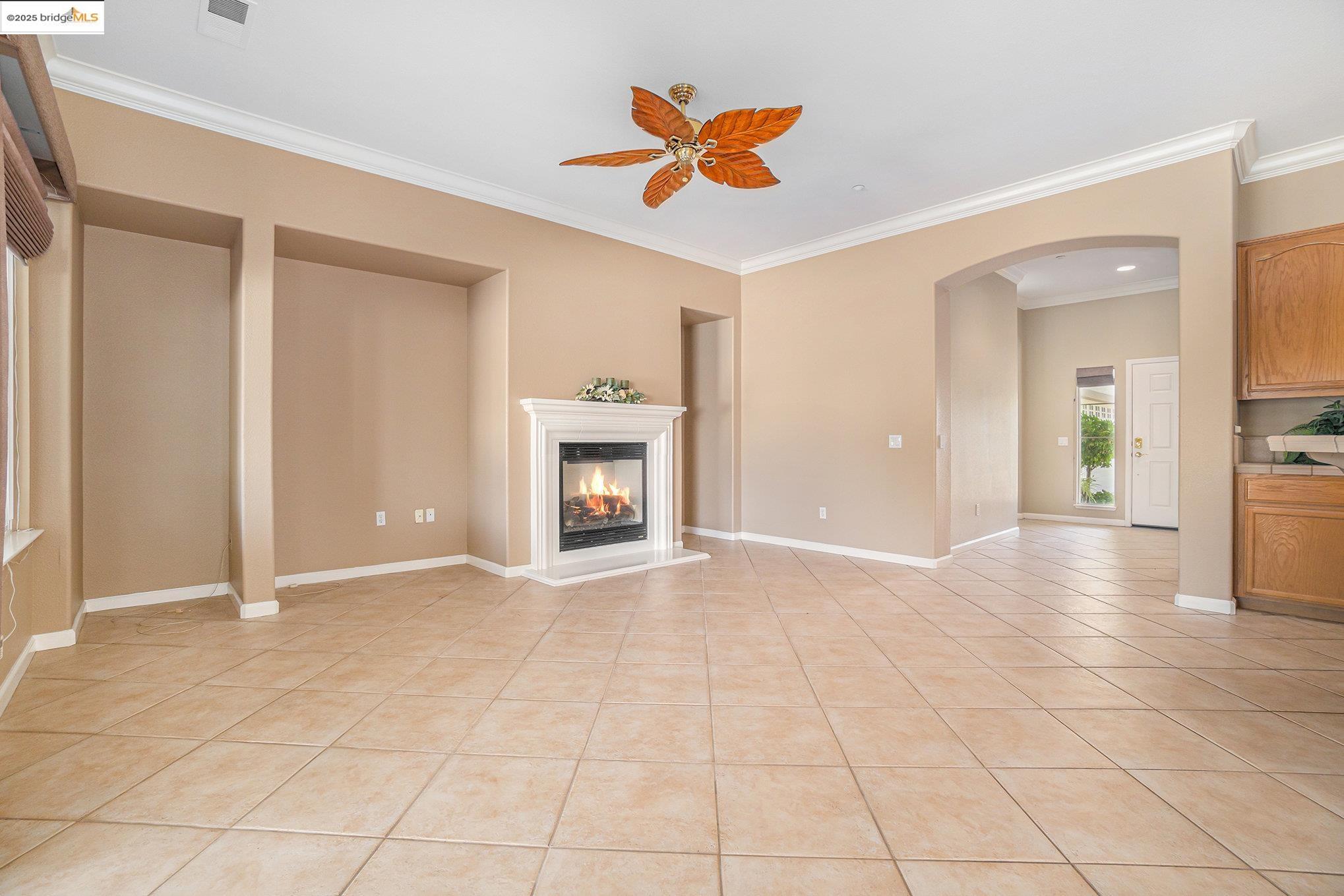 599 Pomona Drive Brentwood, CA 94513 - Photo 3 of 35 Unfurnished living room with ornamental molding, light tile patterned floors, a glass covered fireplace, arched walkways, and ceiling fan
