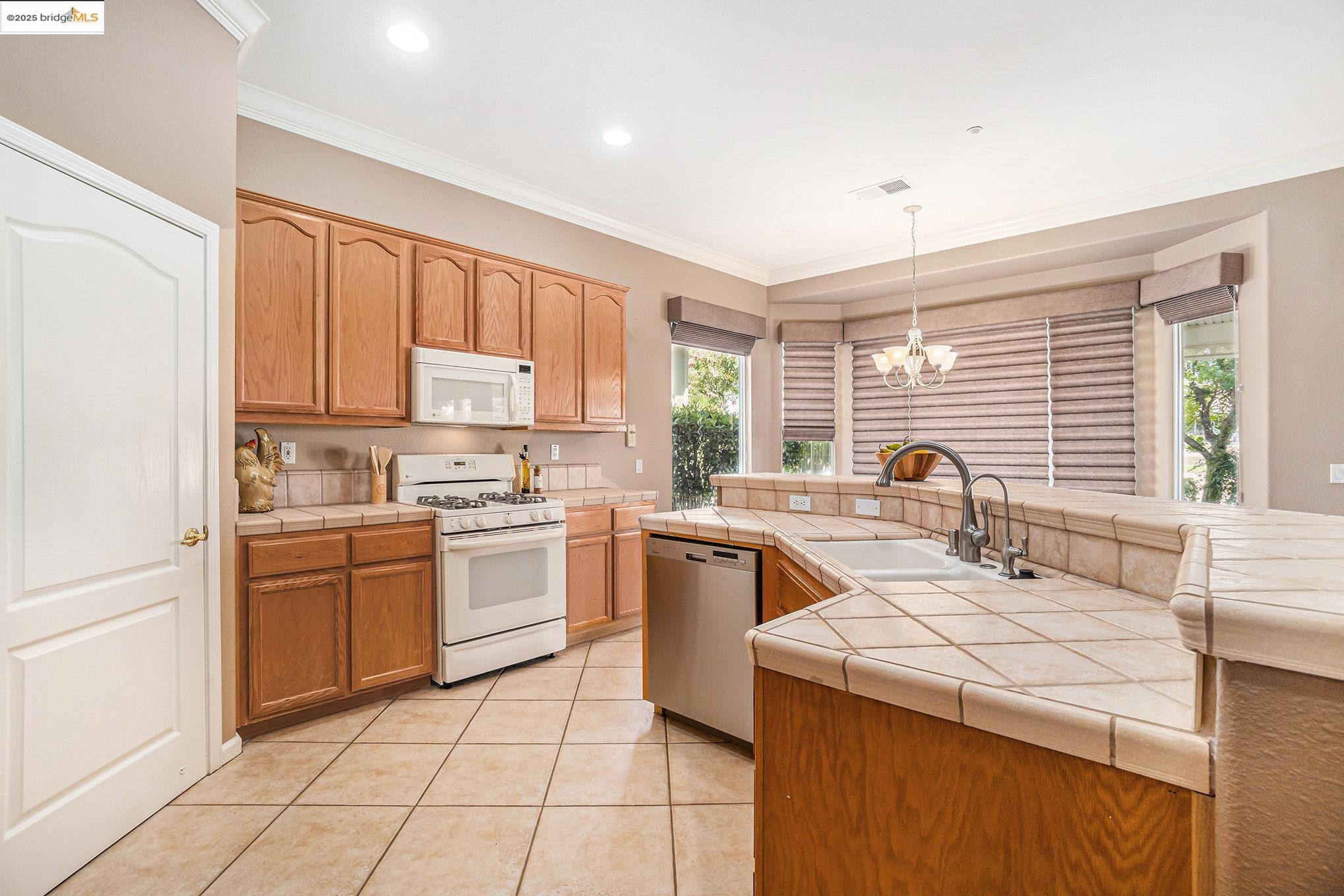 599 Pomona Drive Brentwood, CA 94513 - Photo 6 of 35 Kitchen with white appliances, ornamental molding, a chandelier, tile counters, and light tile patterned floors