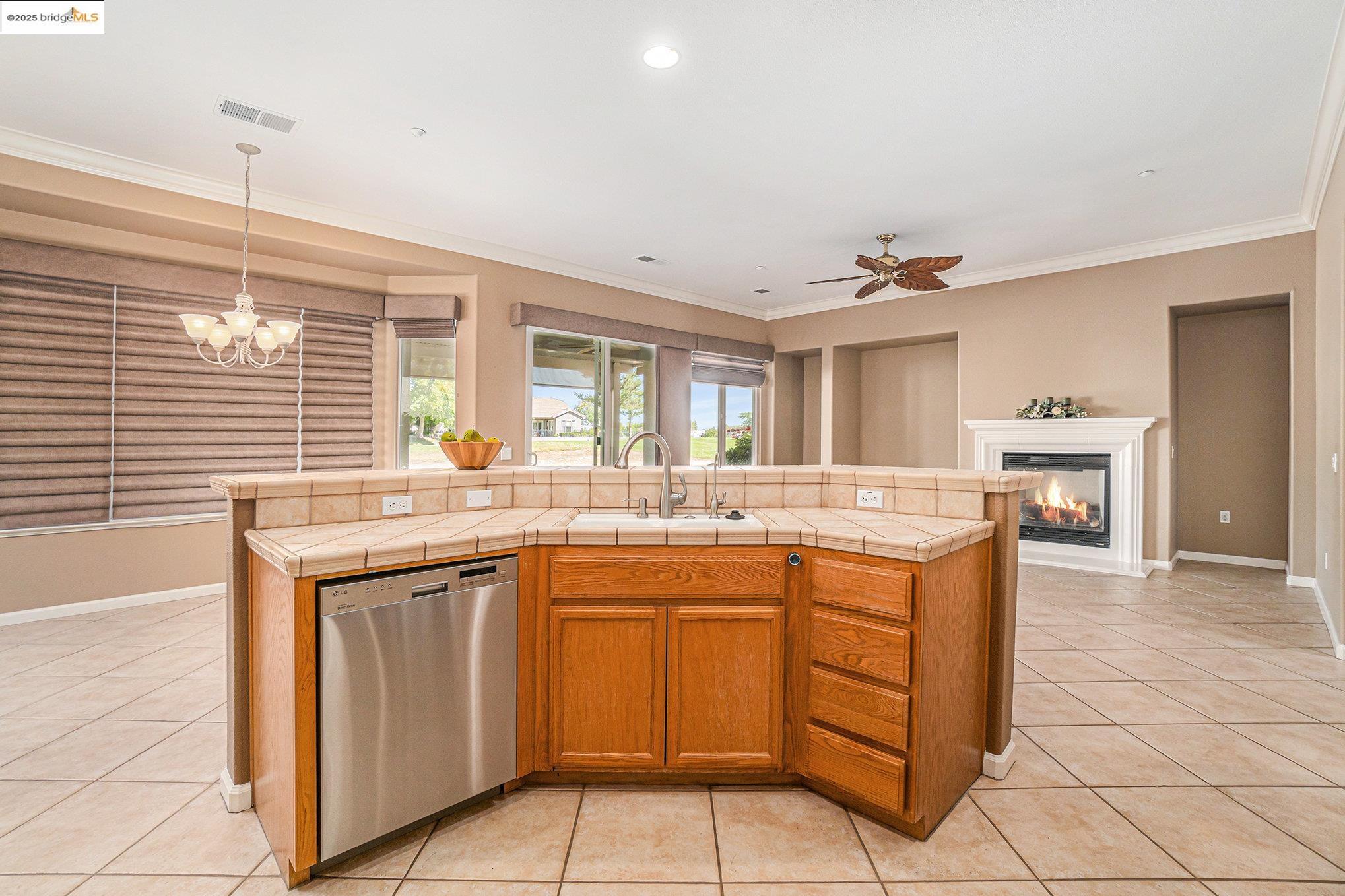 599 Pomona Drive Brentwood, CA 94513 - Photo 7 of 35 Kitchen featuring a glass covered fireplace, dishwasher, light tile patterned floors, crown molding, and a chandelier