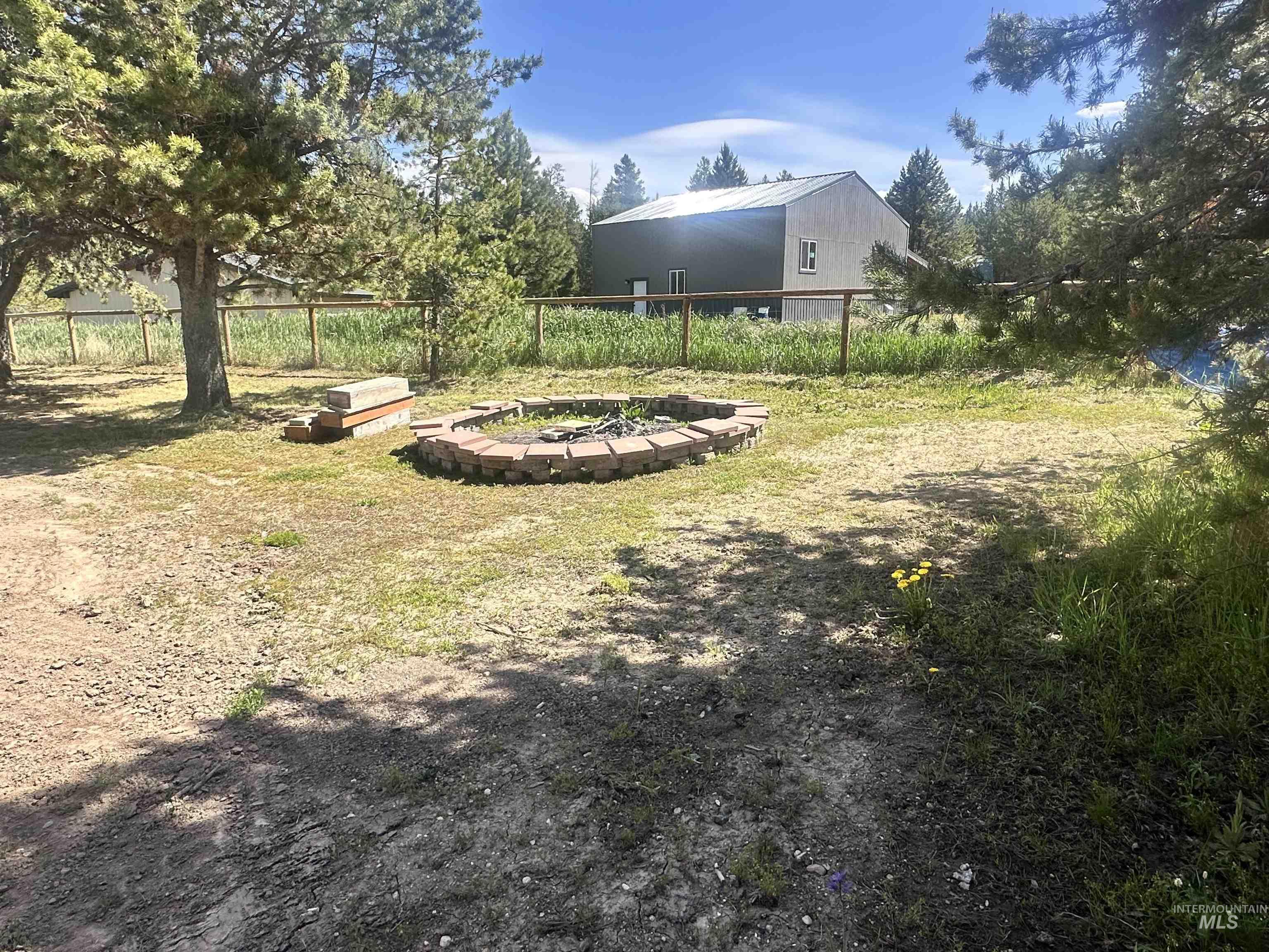 22 West Prospectors Drive Cascade, ID 83611 - Photo 4 of 29 Outdoor space featuring a circular brick fire pit, mature evergreen trees, and a wood fence