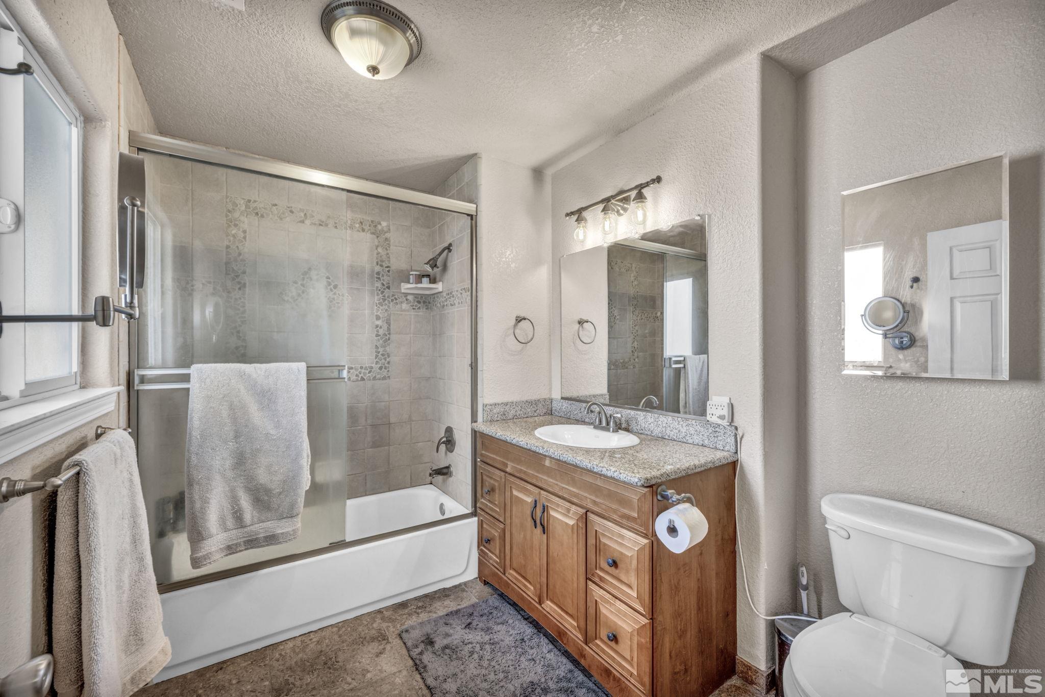 14660 Chamy Drive Reno, NV 89521 - Photo 24 of 38 a bathroom with a granite countertop sink toilet a mirror a vanity and shower