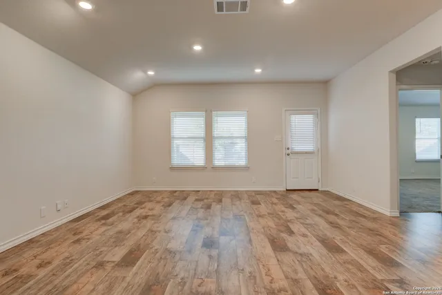 a view of an empty room with wooden floor and window
