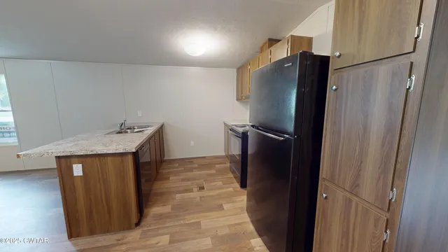 a view of a refrigerator in kitchen and an empty room with wooden floor