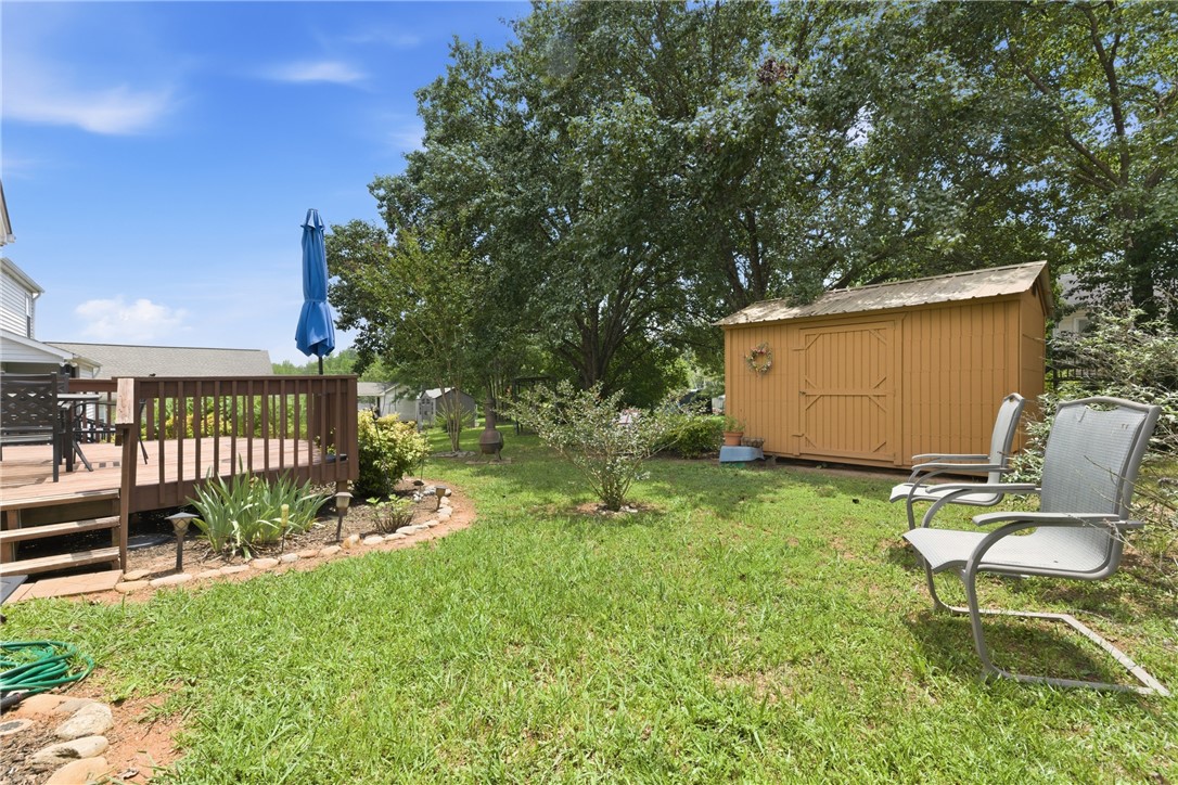 128 Kelly Lane Easley, SC 29642 - Photo 6 of 23 A spacious backyard features a wooden deck and a charming yellow shed, offering ample outdoor living and storage space.