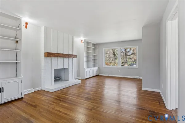 an empty room with wooden floor fireplace and windows
