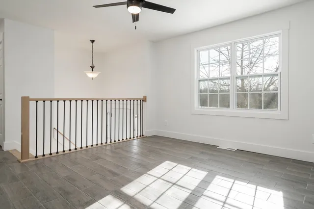 an empty room with wooden floor fan and windows