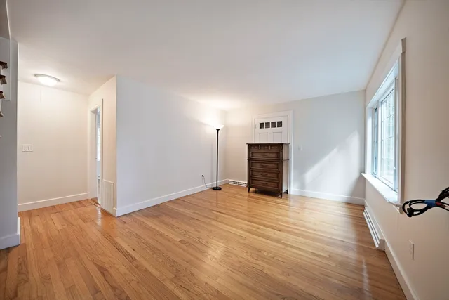 a view of an empty room with wooden floor fireplace and a window