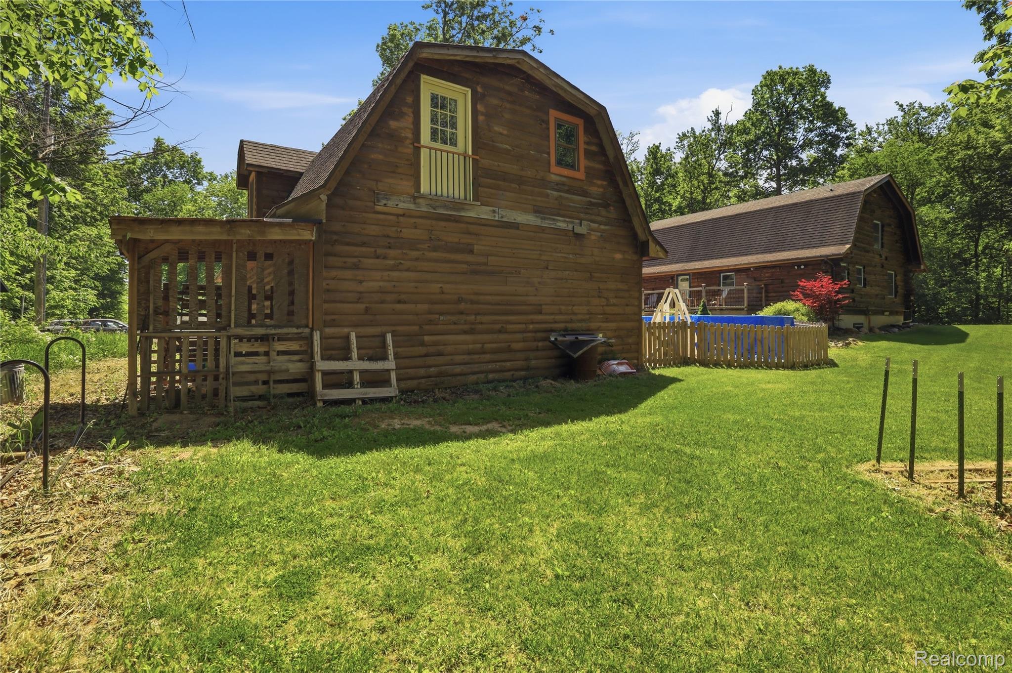 14830 Sheridan Road Byron, MI 48418 - Photo 54 of 74 Wood-sided barn structure featuring a second-story balcony with white railing, covered patio area, and an additional wood-sided building in the background