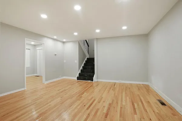 a view of an empty room with wooden floor and a kitchen
