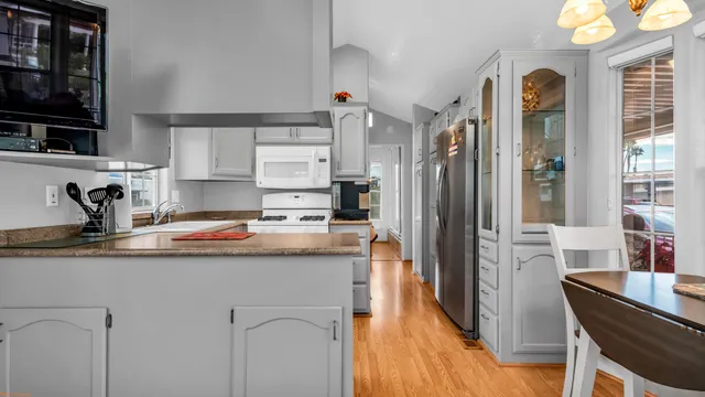 a kitchen with stainless steel appliances granite countertop a refrigerator a sink dishwasher a stove and a dining table with wooden floor