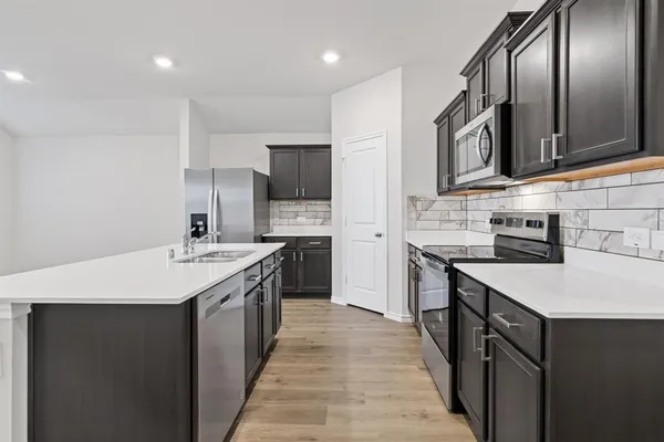 a kitchen with stainless steel appliances a sink dishwasher a refrigerator and a stove top oven with wooden floor