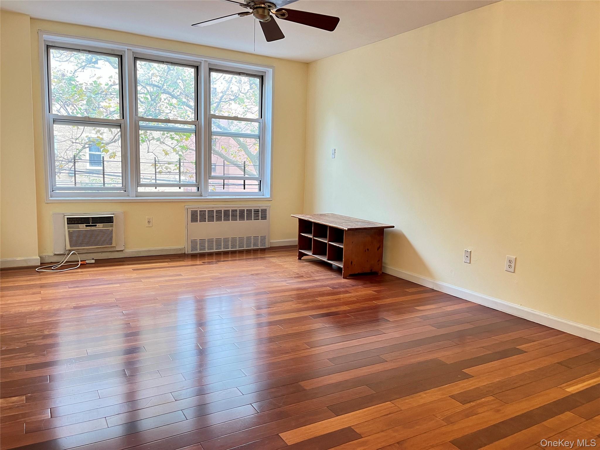 142-15 Franklin Avenue, Unit 3F Queens, NY 11355 - Photo 4 of 15 Empty room featuring light wood-type flooring, radiator heating unit, ceiling fan, and a wall mounted AC