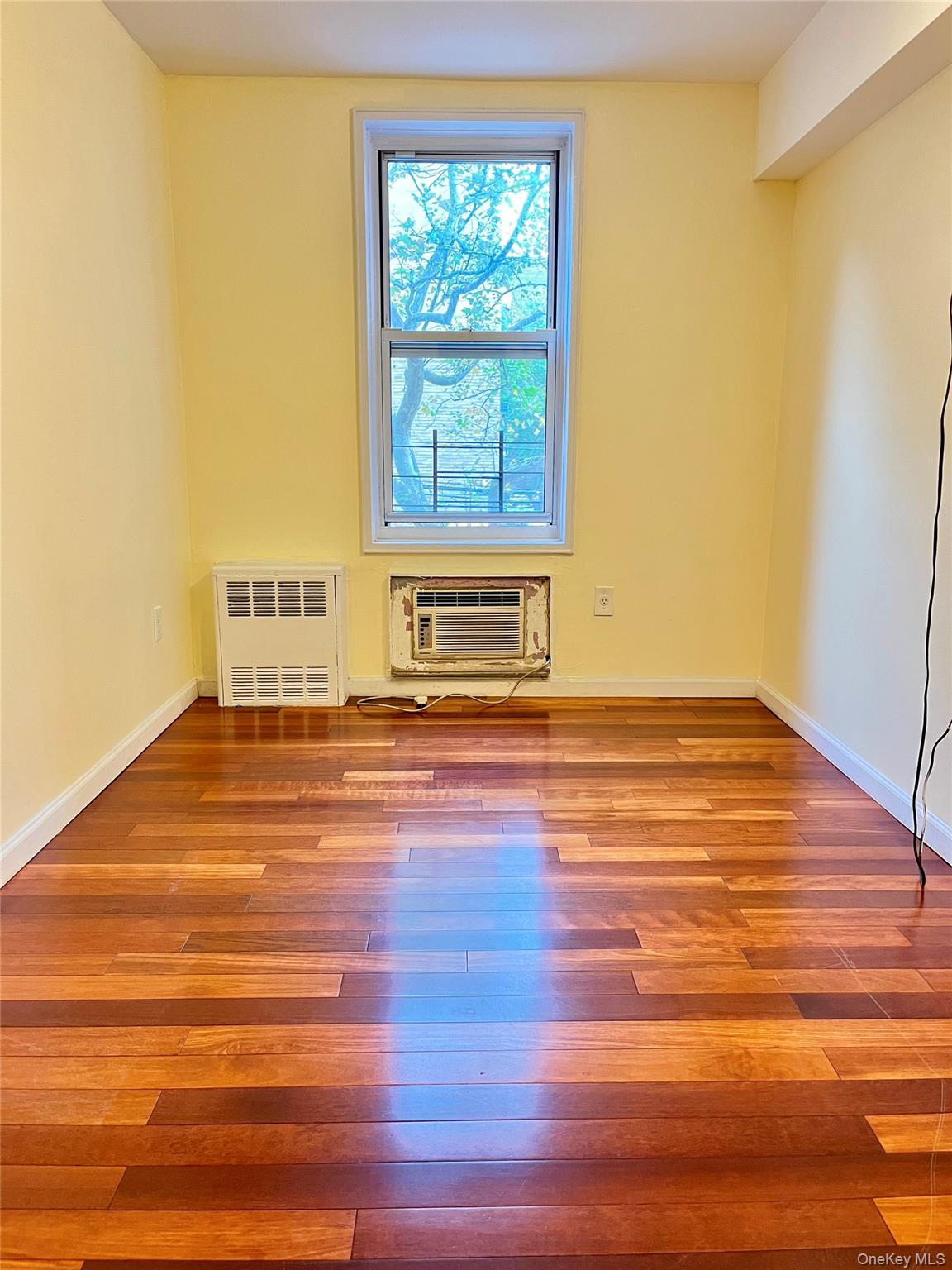142-15 Franklin Avenue, Unit 3F Queens, NY 11355 - Photo 8 of 15 Unfurnished room featuring hardwood / wood-style flooring, radiator heating unit, and a wall mounted air conditioner