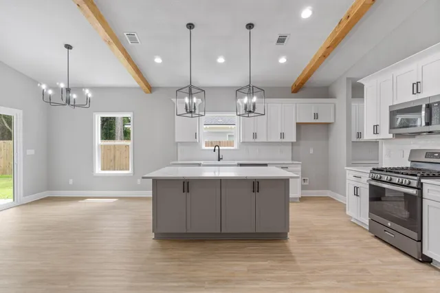 a large kitchen with stainless steel appliances a large stove a sink dishwasher a refrigerator white cabinets and wooden floor