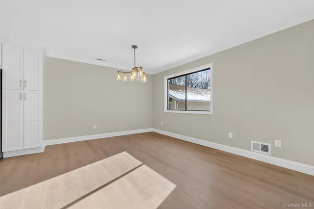 an empty room with wooden floor chandelier and windows