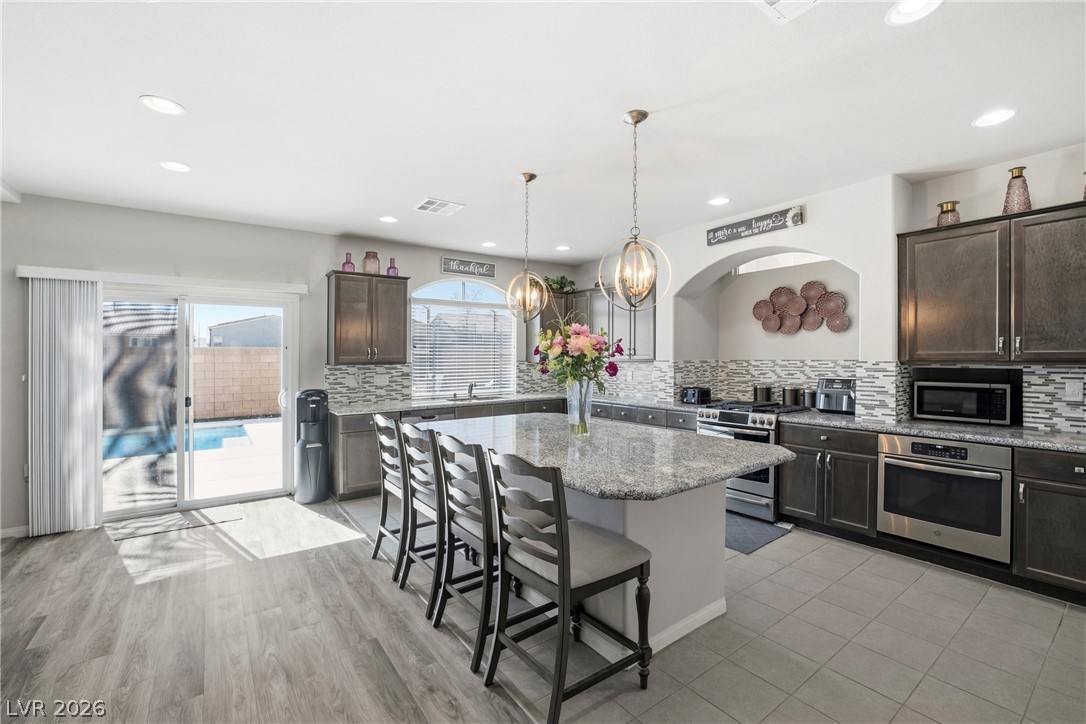 5953 Graystone Ridge Avenue Las Vegas, NV 89141 - Photo 8 of 51 Kitchen with a breakfast bar, stainless steel appliances, light stone countertops, dark wood finish cabinets, and a center island