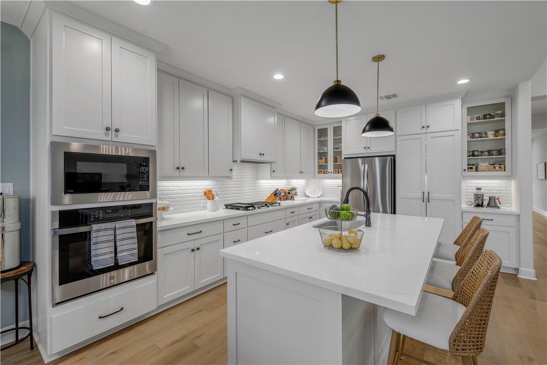 4309 Batona Court Bryan, TX 77802 - Photo 11 of 29 Kitchen featuring light wood-style flooring, a kitchen bar, stainless steel appliances, a center island with sink, and backsplash