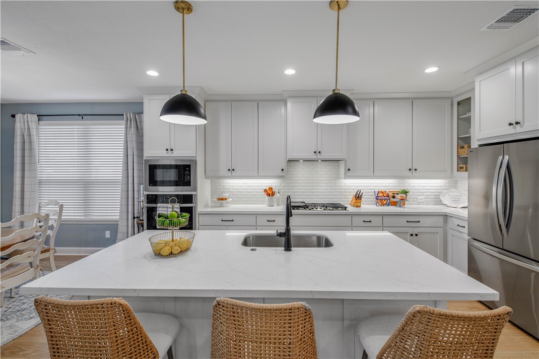 4309 Batona Court Bryan, TX 77802 - Photo 10 of 29 Kitchen featuring light stone countertops, appliances with stainless steel finishes, tasteful backsplash, glass insert cabinets, and a breakfast bar area