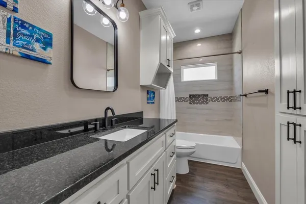 a bathroom with a granite countertop sink a toilet a mirror and shower