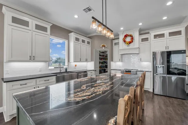 a kitchen with stainless steel appliances granite countertop a stove top oven a sink a dining table and chairs with wooden floor