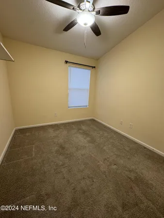 an empty room with a chandelier fan and windows