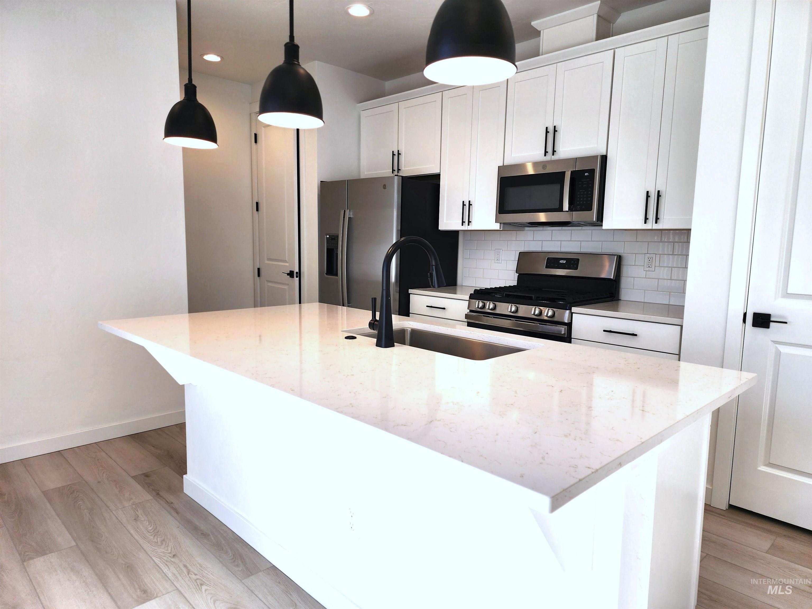 12267 West Endsley Street Star, ID 83669 - Photo 4 of 18 Kitchen featuring appliances with stainless steel finishes, white cabinets, a kitchen island with sink, backsplash, and light stone counters