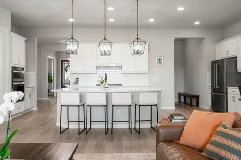 a kitchen with stainless steel appliances kitchen island granite countertop a refrigerator a stove a kitchen island a dining table and chairs with wooden floor