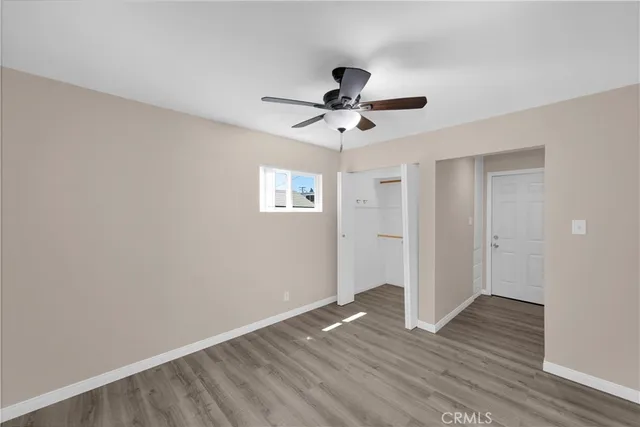 a view of an empty room with wooden floor and a ceiling fan