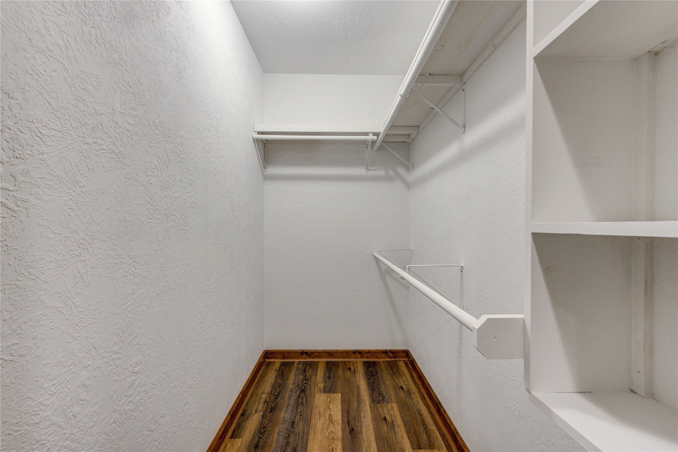 8805 Sun Oil Road Brenham, TX 77833 - Photo 36 of 50 Spacious walk-in closet with ample shelving and hanging space, featuring elegant wood flooring and bright white walls for a clean, organized look.