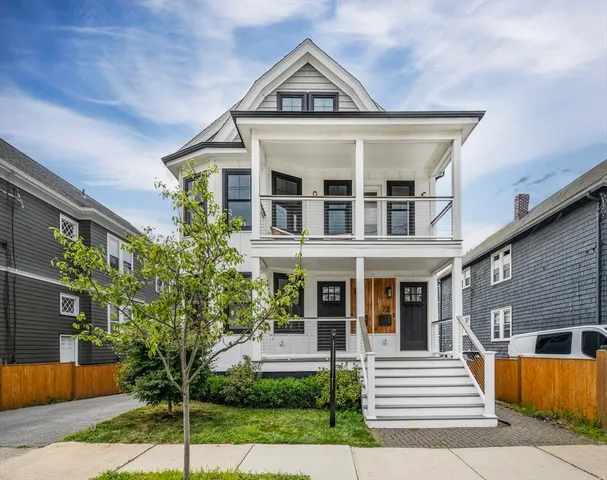 a view of a white house with a small yard plants and large tree