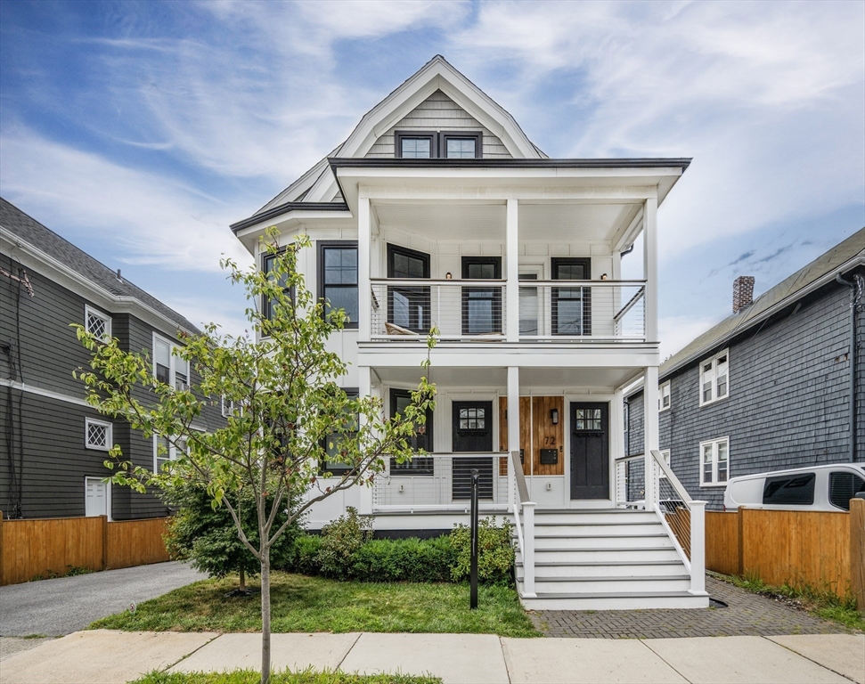 a view of a white house with a small yard plants and large tree