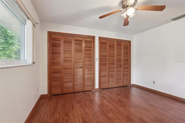 an empty room with wooden floor chandelier fan and windows