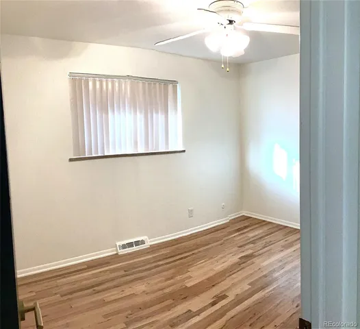 an empty room with wooden floor fan and window