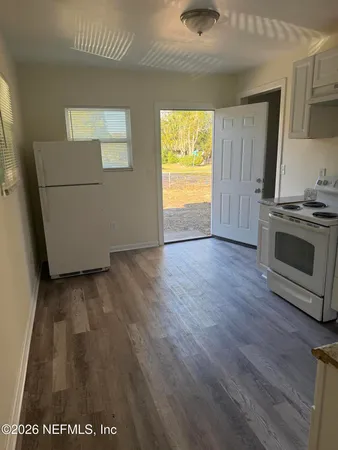an empty room with wooden floor and a kitchen